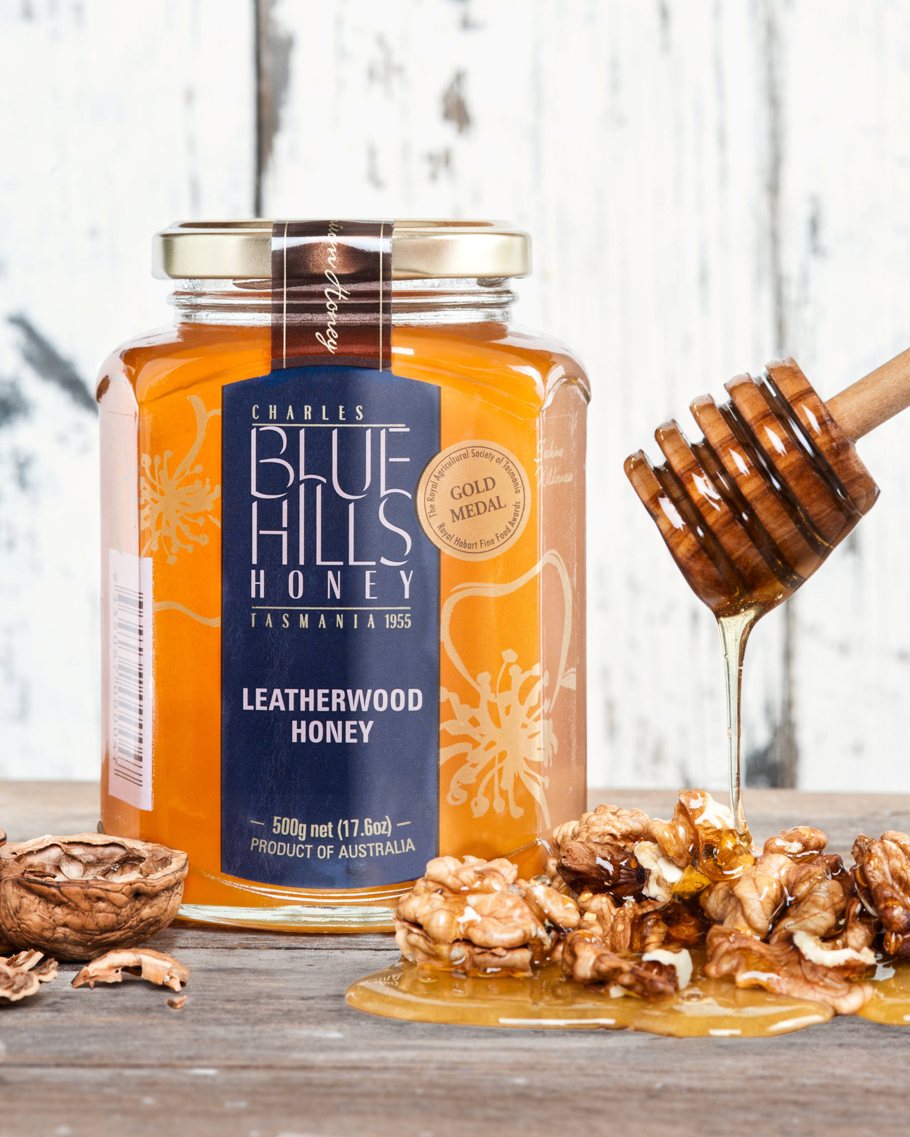 Large jar of Blue Hills Leatherwood honey with honey dripping off a wooden honey stirer onto some shelled walnuts.  Photo: Blue Hills Honey.