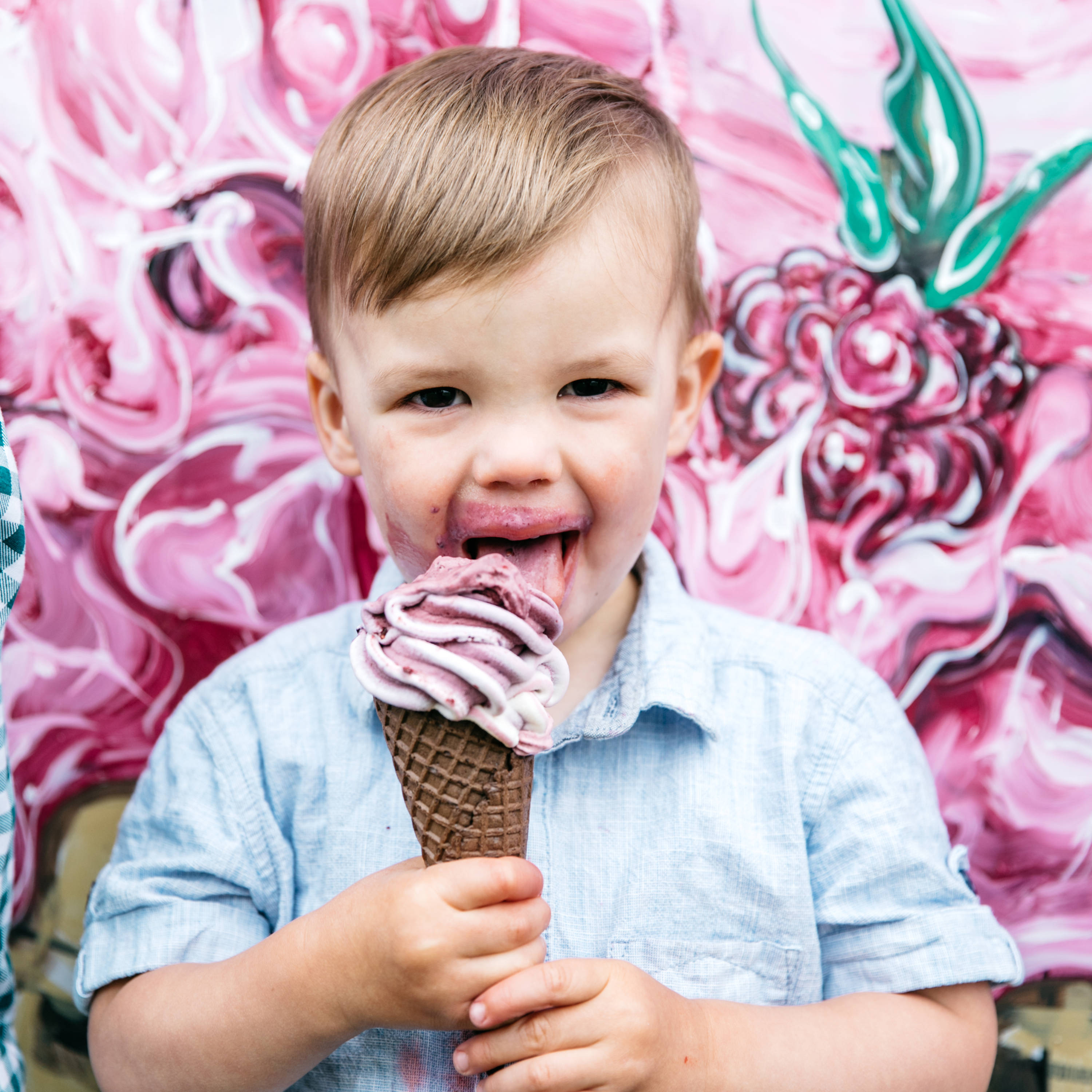 Little boy licking a large swirl of berry ice cream in a cone, with ice cream all around his mouth. Photo: Melanie Kate Photography.