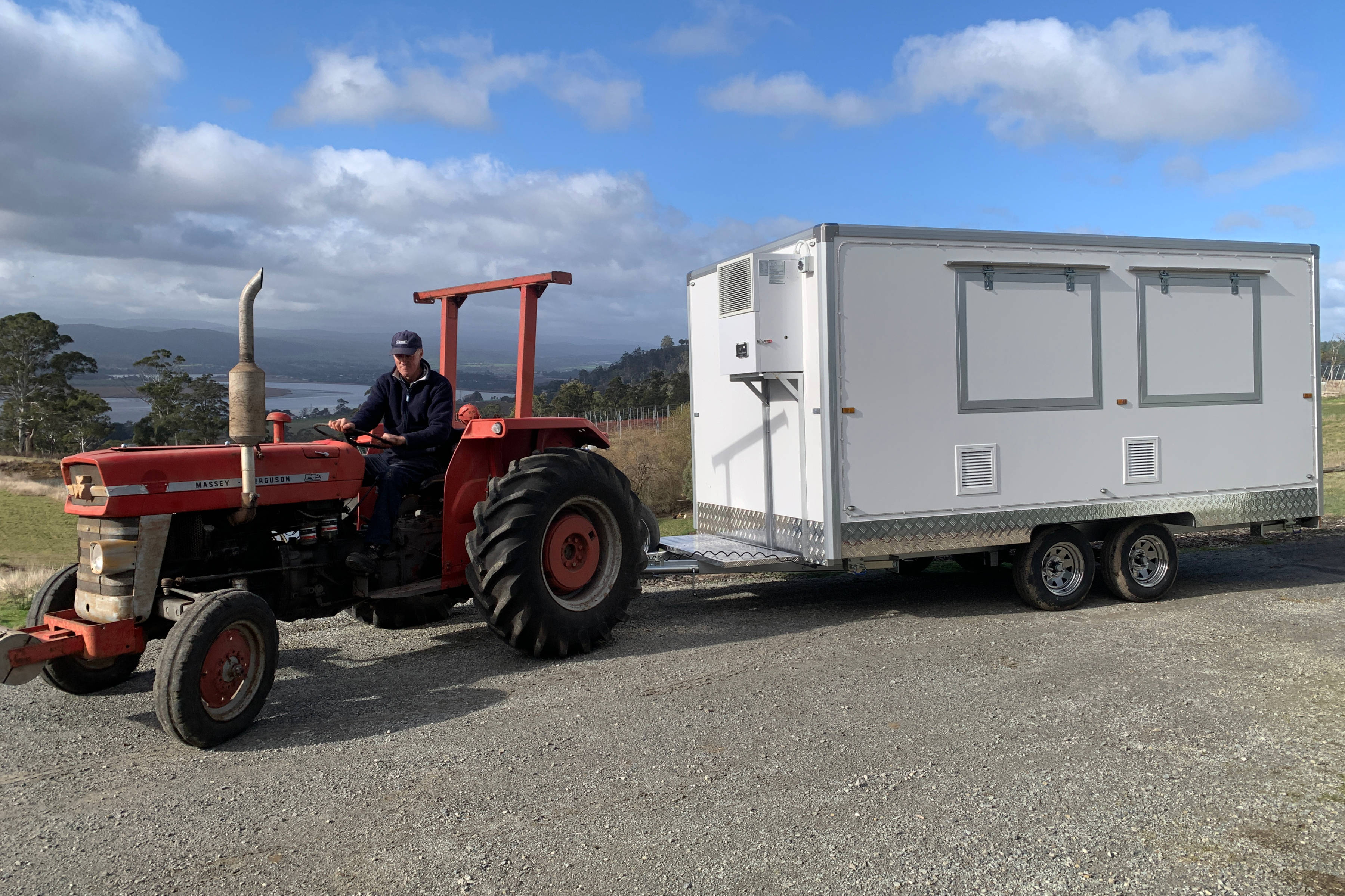 Man driving a red tractor and towing a white food van. Photo: Rosevears Farm.
